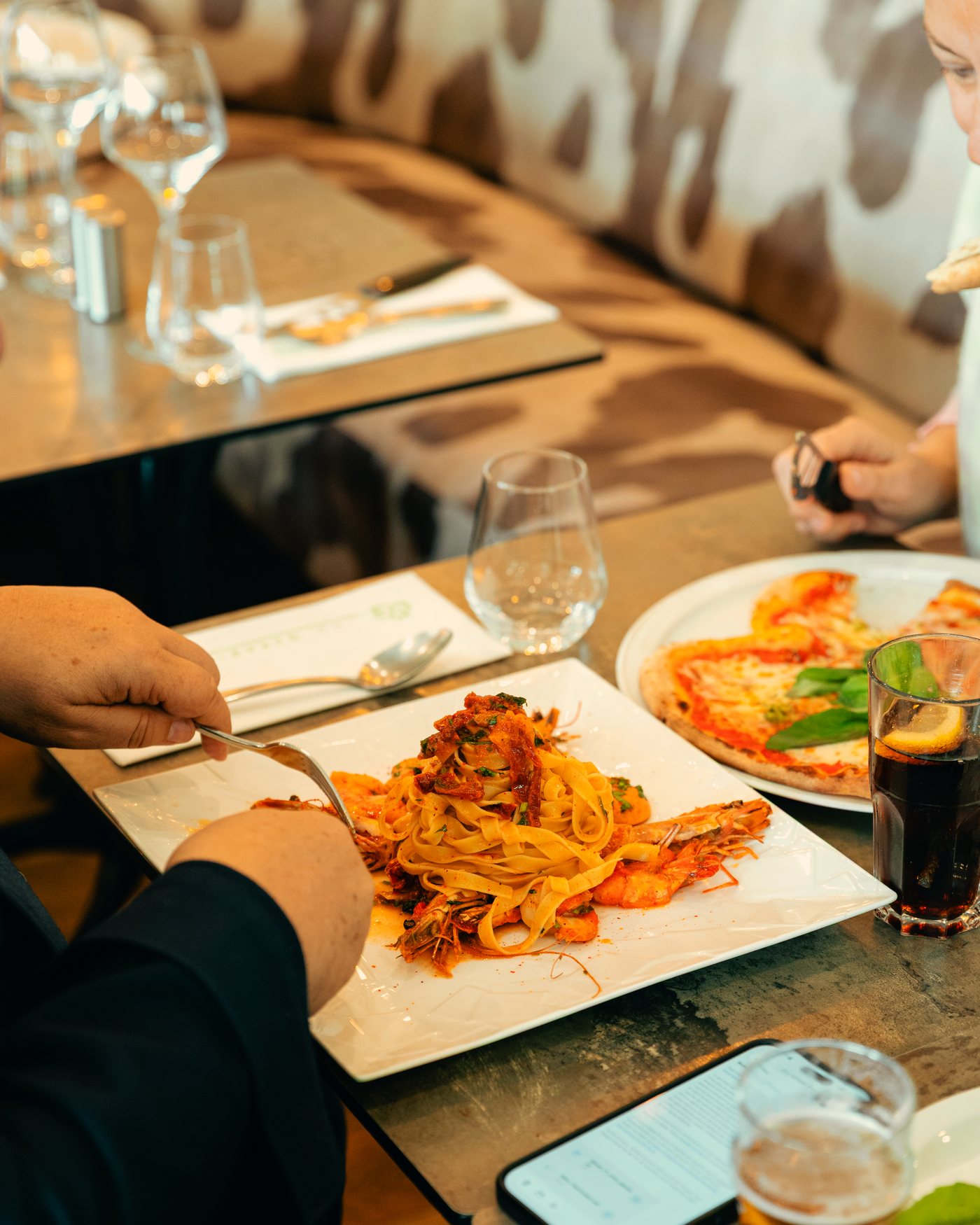 Une convive coupe des tagliatelles aux gambas à table.